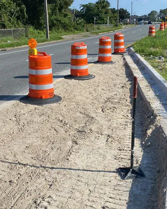 Newly poured concrete curb and gutter running alongside a roadway, with work-zone cones in place.