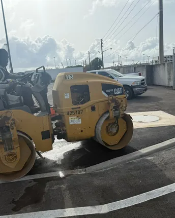 An asphalt roller compacting a freshly paved surface at a project site.