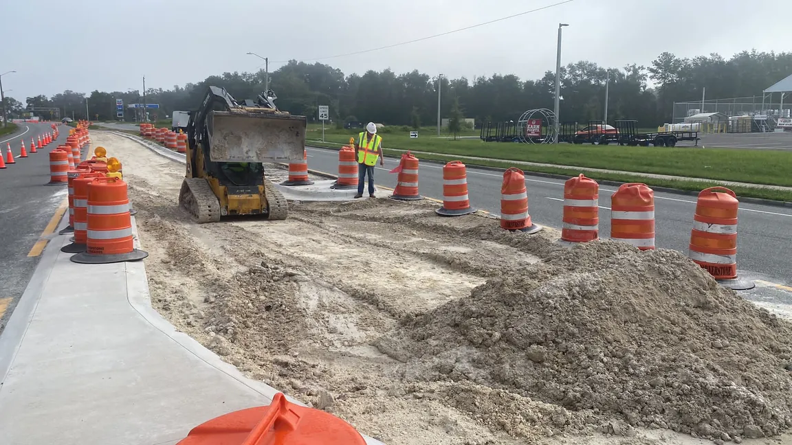 A Goal Builders and Paving crew grading and paving a new roadway with a skid steer loader and traffic cones on an active Florida jobsite.